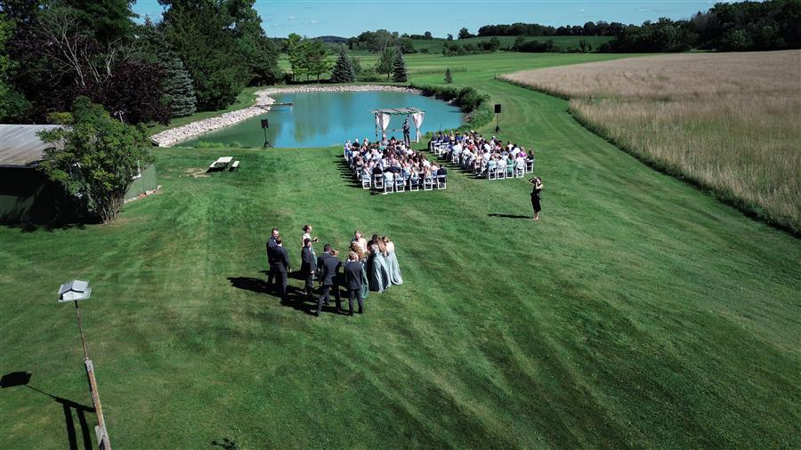 Aerial view of a wedding ceremony in progress with guests seated on a lawn beside a pond