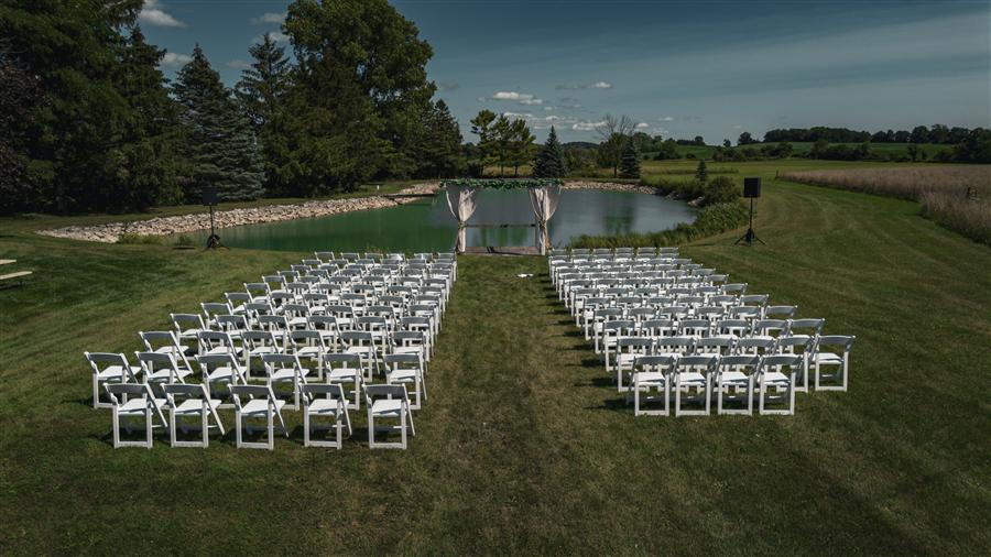 Empty rows of white chairs set up for an outdoor wedding ceremony beside a pond